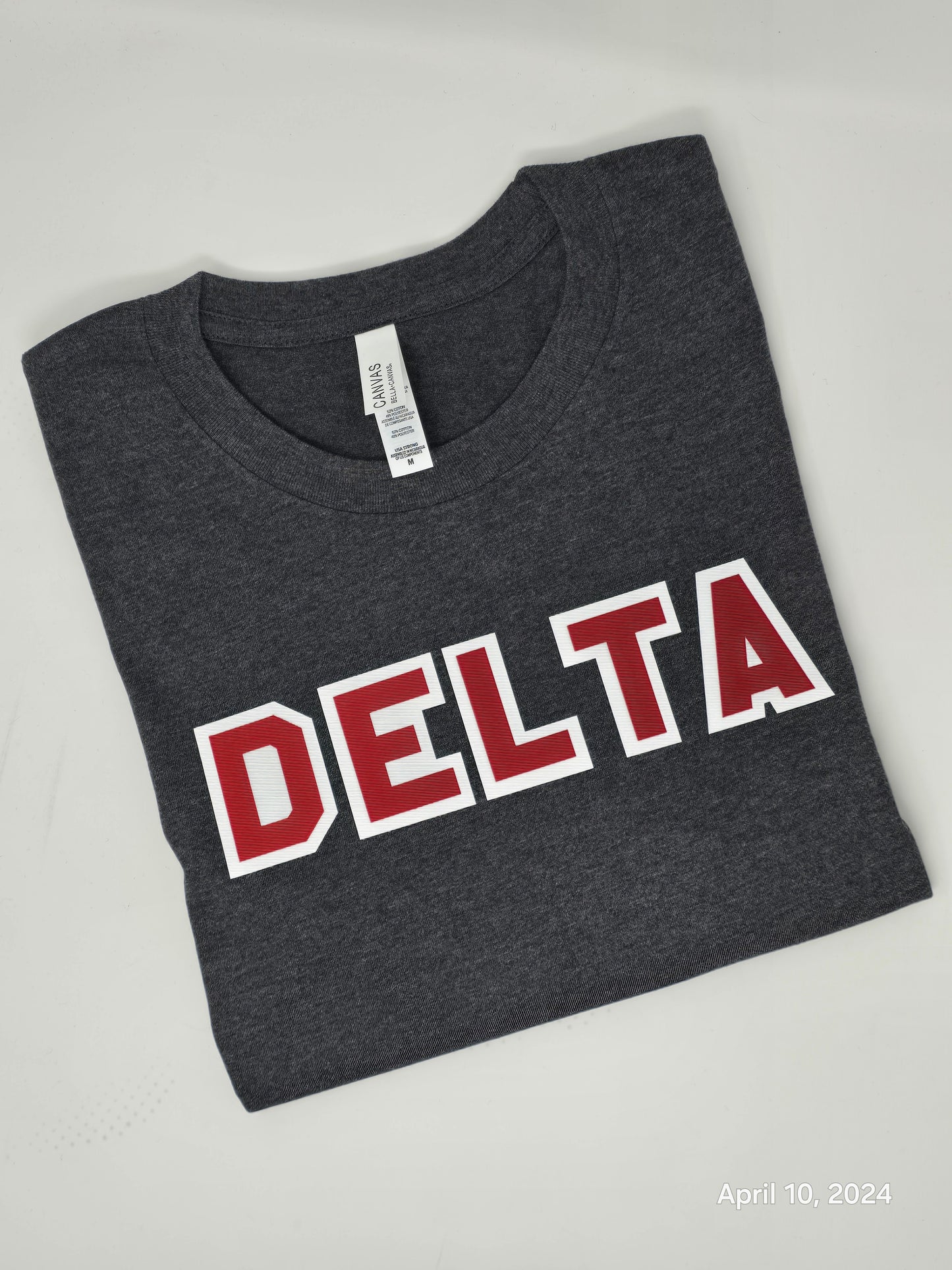 A charcoal gray Delta Sigma Theta Sorority Inc. twill-lettered tee with red and white text laid flat on a surface.