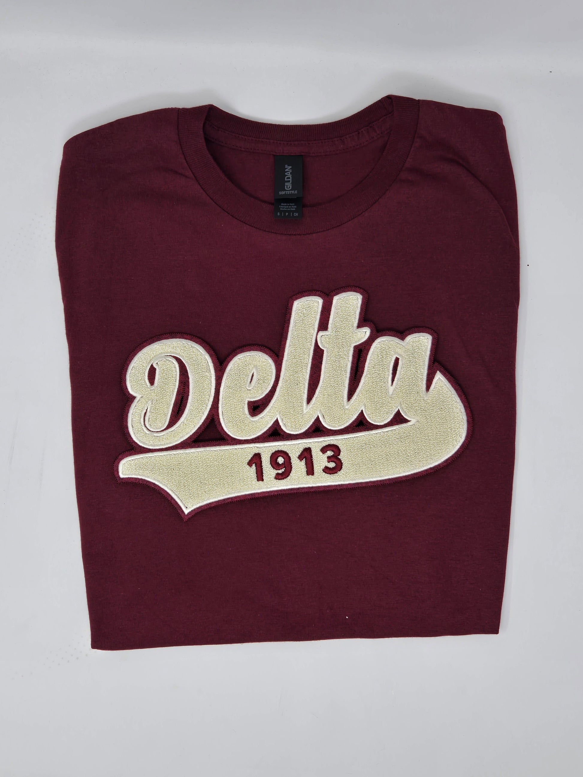 A maroon colored t-shirt with 'Delta 1913' embroidered in cream-colored chenille text on the front.