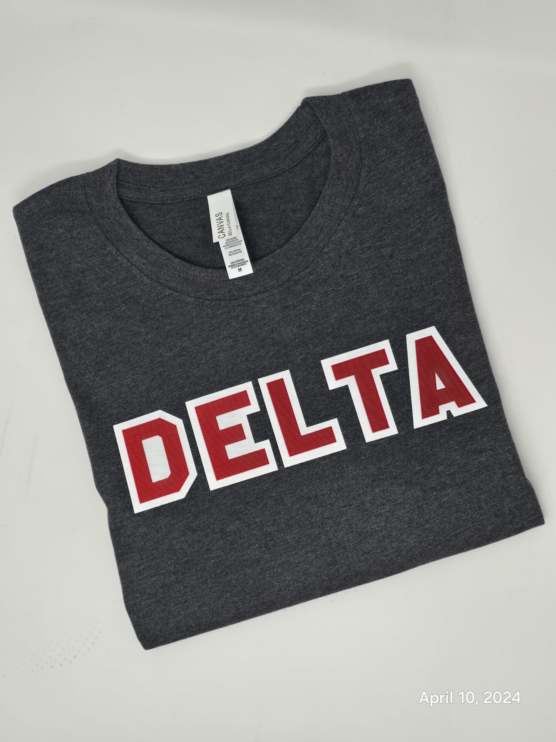 A charcoal gray Delta Sigma Theta Sorority Inc. twill-lettered tee with red and white text laid flat on a surface.