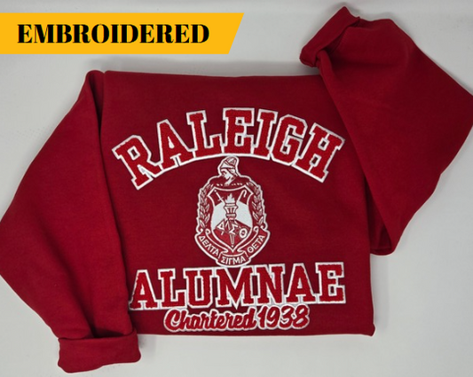 A red sweatshirt with 'RALEIGH ALUMNAE' and 'Chartered 1938' embroidered on it, representing the Delta Sigma Theta Sorority, Inc.